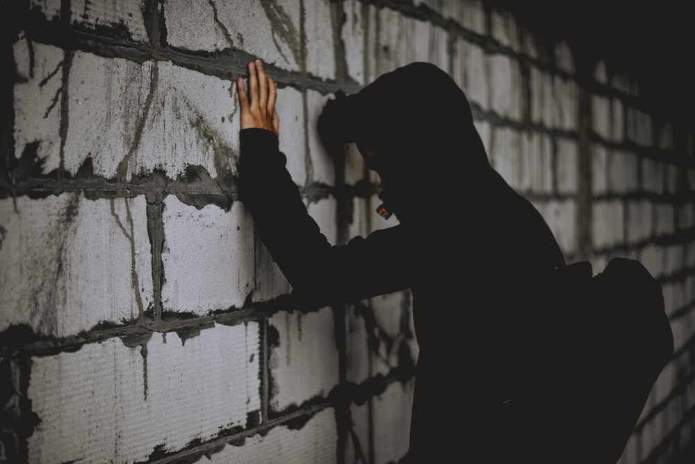 An adolescent leaning against a wall in shadow
